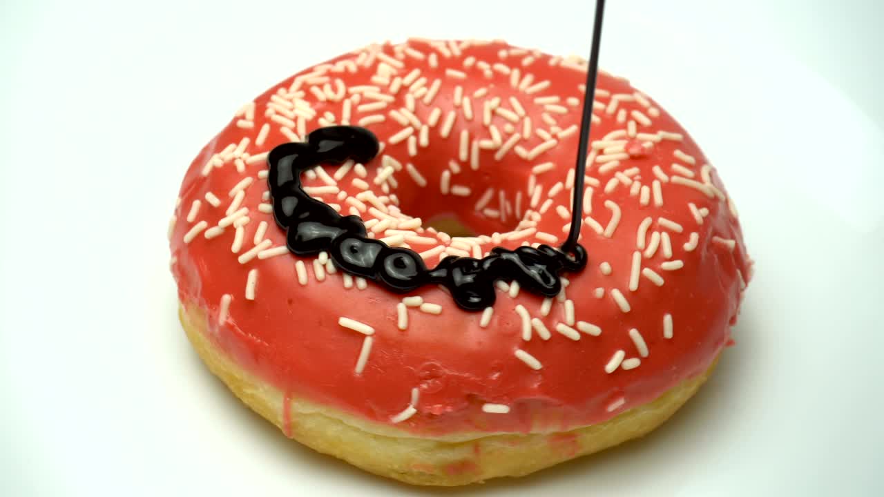 deliciosa rosquilla roja dulce girando en un plato. vertiendo chocolate. vista lateral. rosquilla salpicada brillante y colorida macro disparo de primer plano girando en una placa blanca.