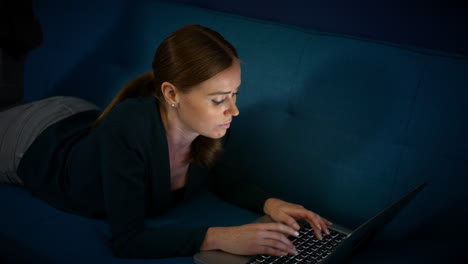 an attractive woman lying on a sofa using a laptop at night