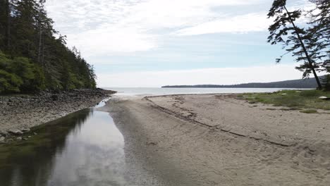 calm aerial dolly shot over a stream leading out to coastal beach with sand, sandpit, canada