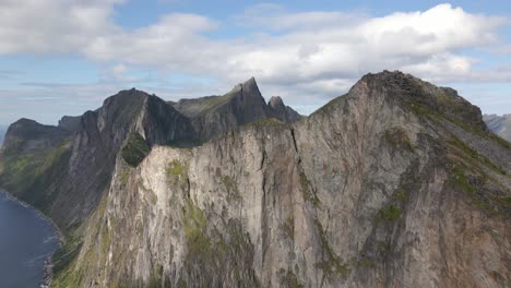 Aerial-tilt-up-of-giant-mountain-range-on-Senja-Island-with-coastline-in-Norway-during-cloudy-day