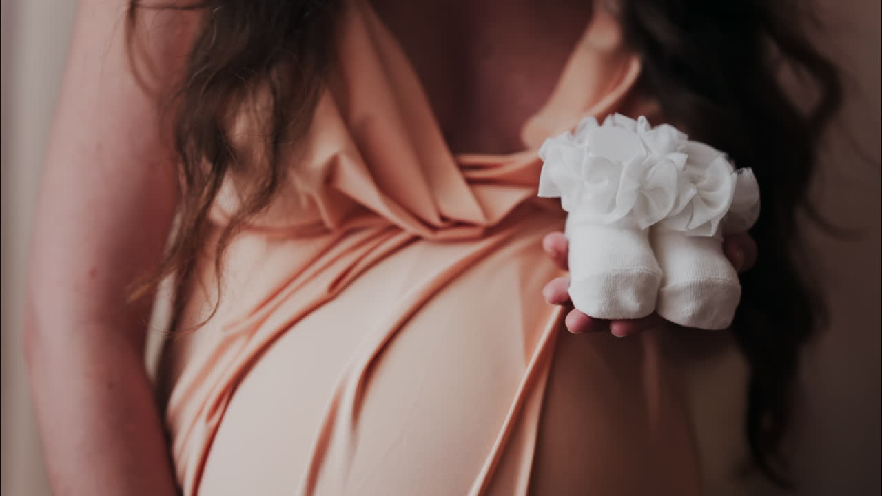 Close up of a pregnant woman holding and playing with white baby socks on her belly