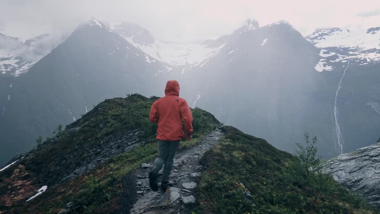 Man wearing a red jacket, running fast over a small path on top of the mountains.