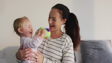 Caucasian-mother-playing-with-her-baby-holding-a-toy-sitting-on-the-couch-at-home