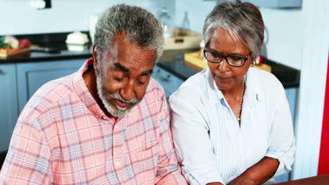 Senior-couple-discussing-over-bills-in-kitchen