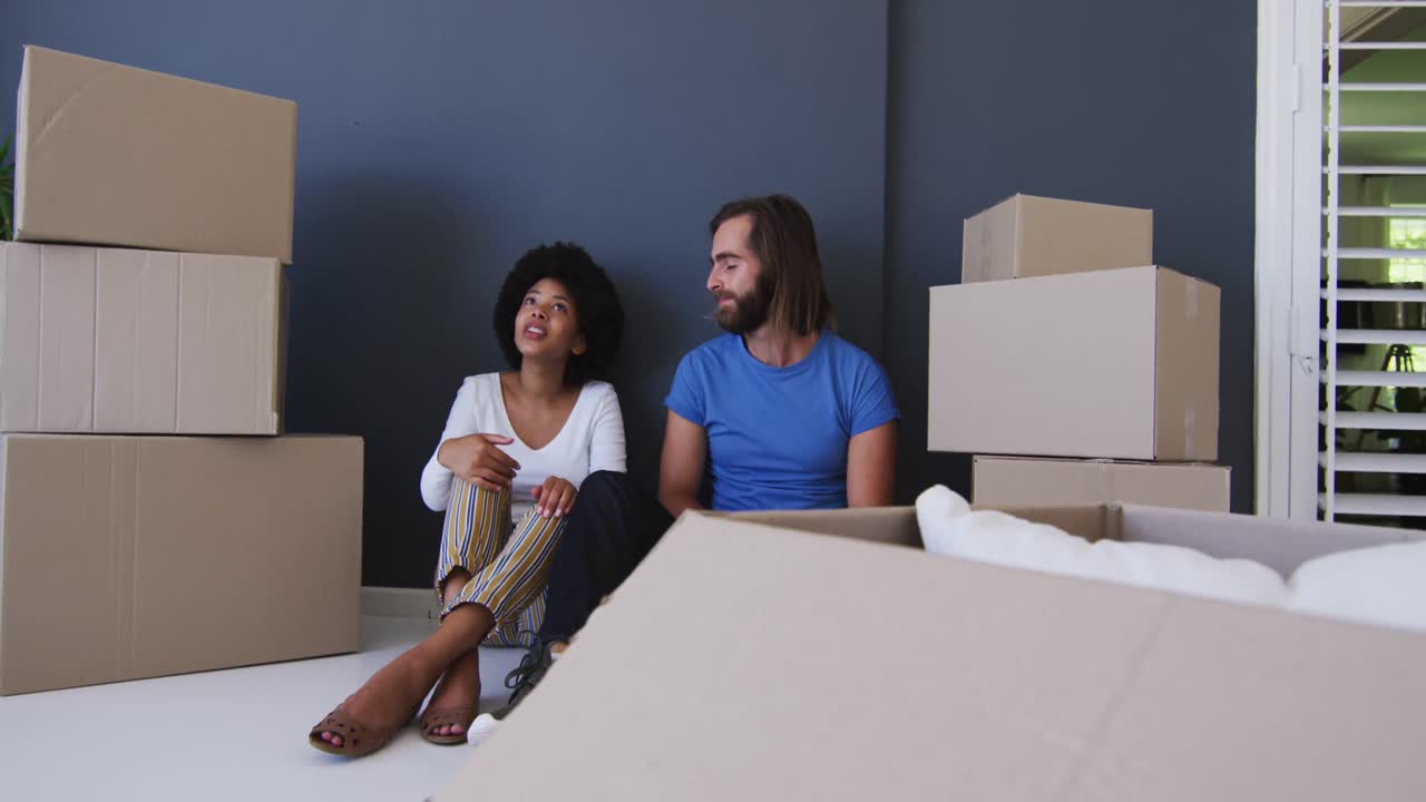 Mixed race couple sitting in between cardboard boxes at new apartment house