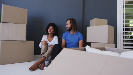 Mixed-race-couple-sitting-in-between-cardboard-boxes-at-new-apartment-house