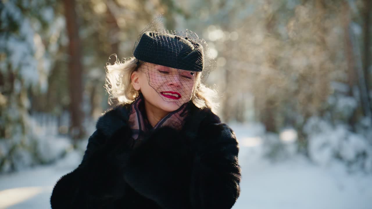 Donna elegante in pelliccia che espira vapore in una foresta invernale innevata