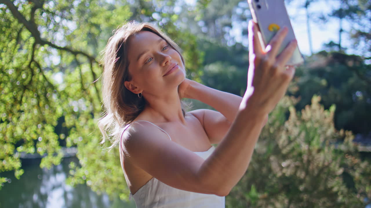 Flirting girl making selfie cellphone posing at lake shore in dress closeup