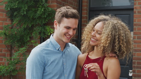 portrait of excited young couple standing outside new home holding keys together