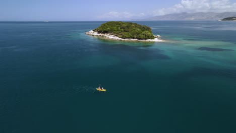 Aerial-circling-people-kayaking-around-beautiful-Ksamil-islands,-Albania