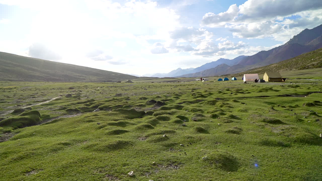 Handheld shot as walking around a tent camp, Nimaling in the Himalayas on an open green field