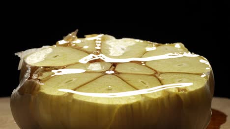 close up pouring oil over a garlic cloves. black background