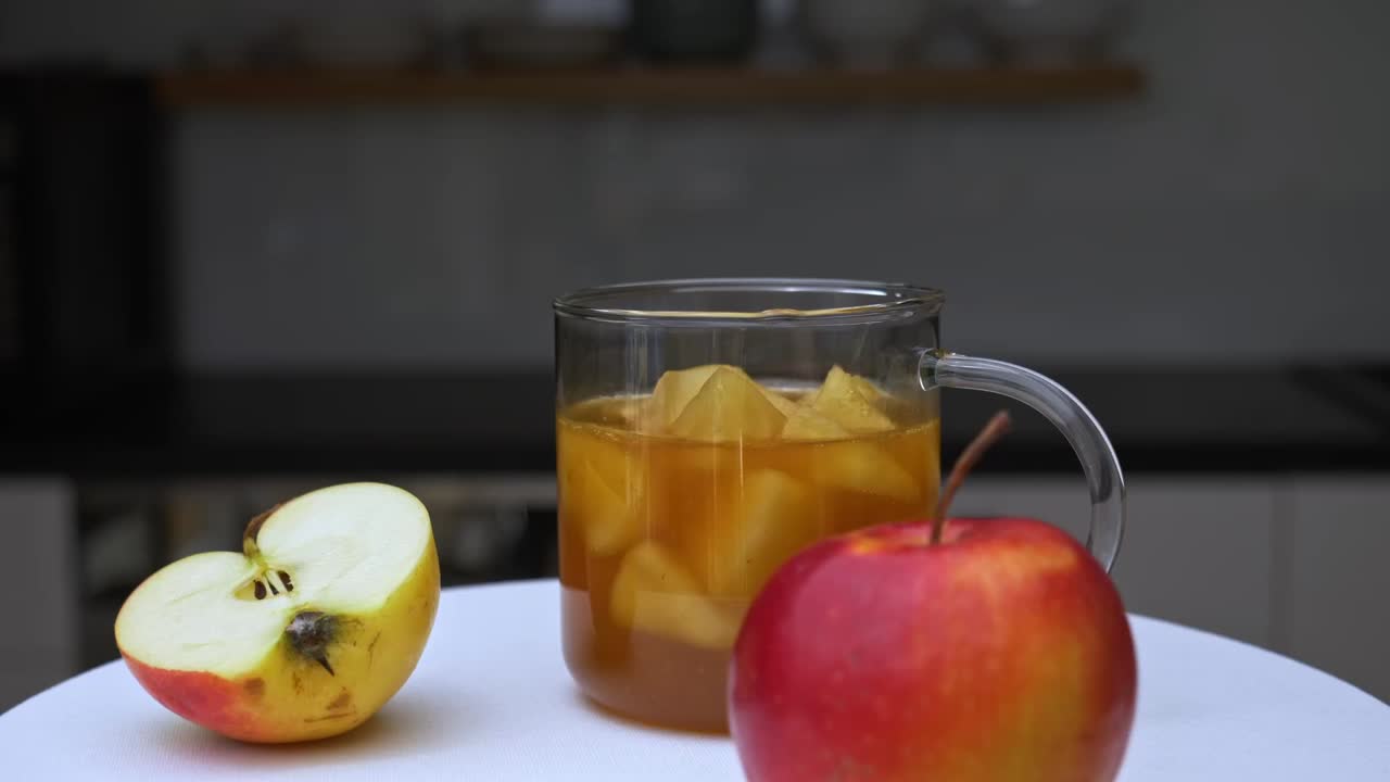 A warm apple beverage spins around on a plate with a halved and whole apple on either side