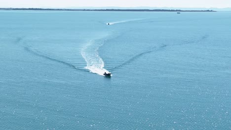 front aerial view of motorboat piloting through open water leaving wake