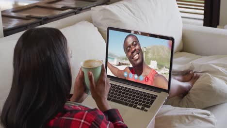 Mixed-race-woman-sitting-on-sofa-using-laptop-making-video-call-with-male-friend
