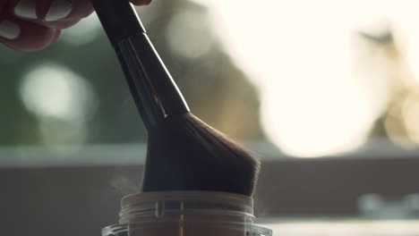 Close-up-of-makeup-artist-dipping-brush-in-a-small-container-of-powdered-blush