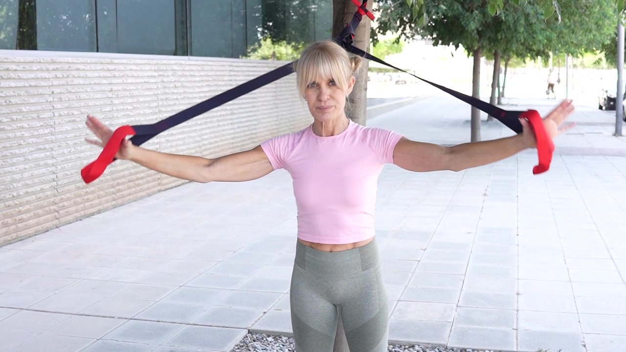 Una donna sta facendo un allenamento all'aperto usando fasce di resistenza con maniglie rosse.