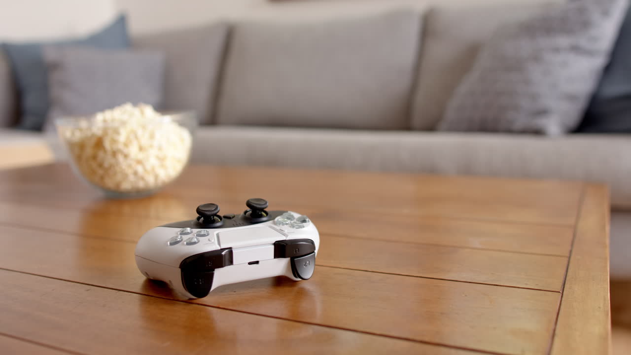 Video game controller on wooden table with bowl of popcorn in living room, at home, copy space