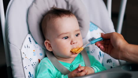 baby nutrition from spoon with healthy food. cute toddler sitting in a special chair eating vegetable puree.