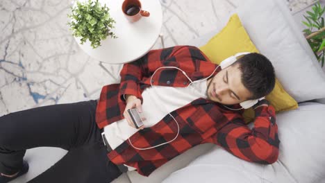 joven escuchando música con auriculares descansando en un cómodo sofá y feliz.