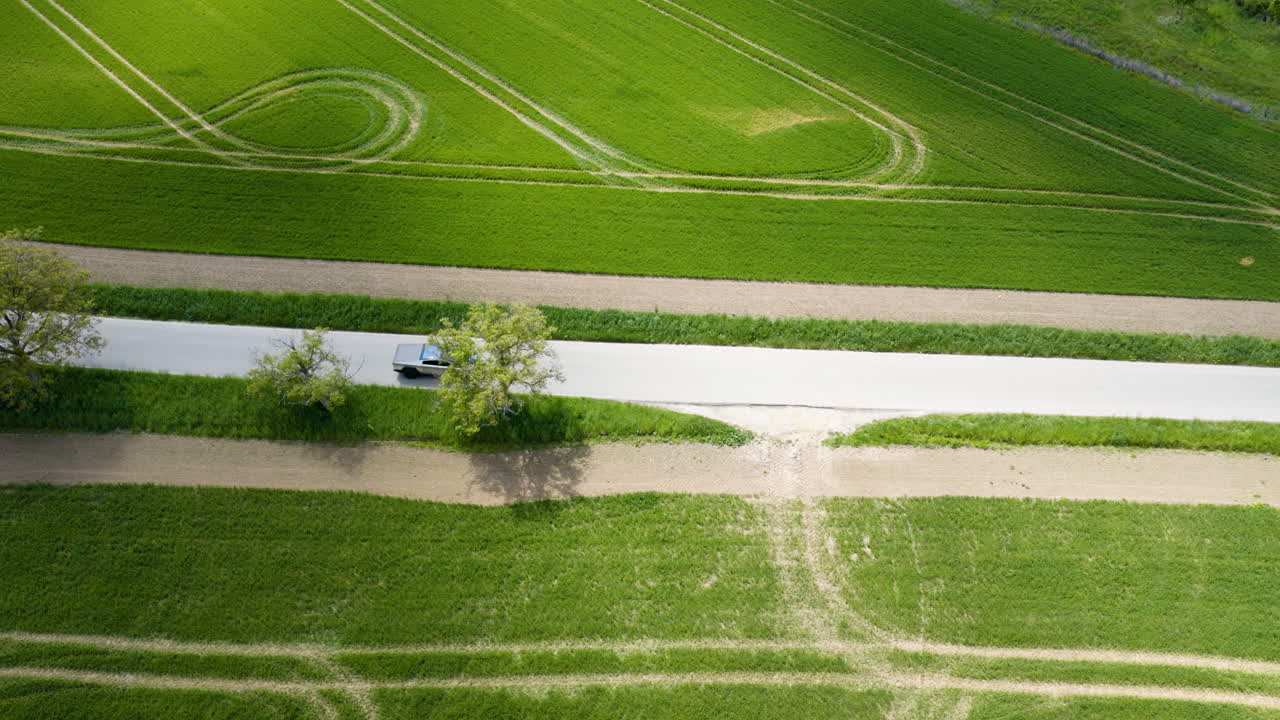Drone tracking a modern EV driving on a asphalt road between countryside fields