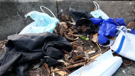máscaras faciales desechables sucias del virus de la corona y guantes de látex entre basura sucia de cigarrillos en el bordillo de la calle empujar hacia adelante