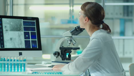 Female Scientist Using Microscope and Computer in Lab