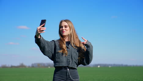 Attractive girl doing video call in nature. Young blogger woman talking on a phone camera while walking on a green meadow in a sunny day.