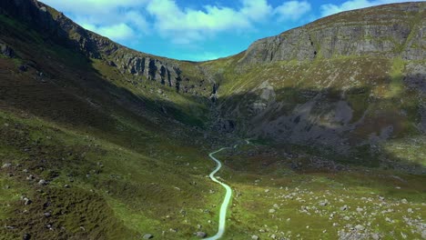 Aerial-view-of-a-rugged-mountain-valley-and-winding-path-leading-to-a-rocky-waterfall-in-the-South-of-Ireland-during-summer