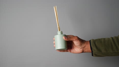 hand holding a green diffuser with wooden sticks