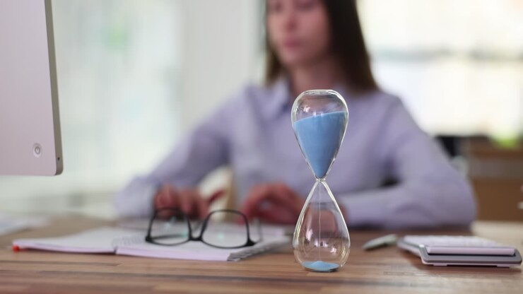 Hourglass on an Office Desk with Person Working