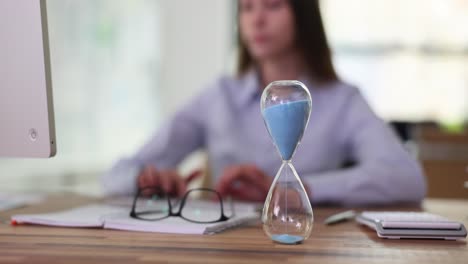 hourglass on an office desk with person working