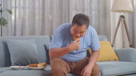 a fat asian man weighing himself while eating fast food having fried chicken in the living room at home