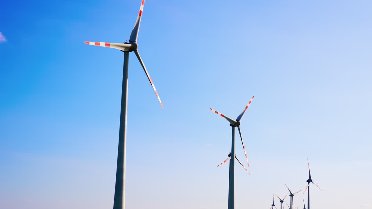 Turbines harness energy. Rows of wind turbines stand tall under a bright blue sky, harnessing renewable energy in an open landscape