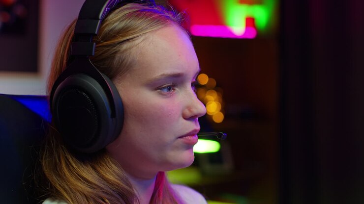 Junge Gamerin mit Kopfhörern und Mikrofon, konzentriert beim Videospielen