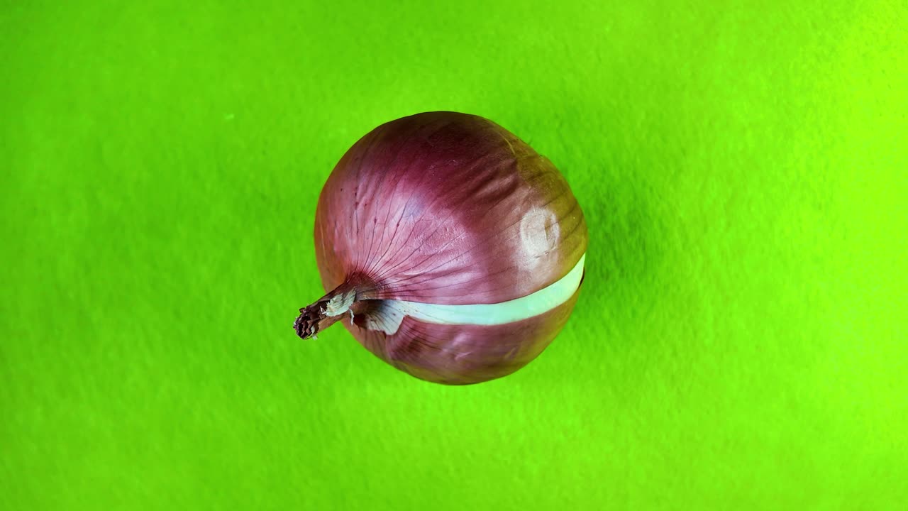Whole red onion resting on a vibrant green background, showcasing a striking contrast that highlights its rich color and natural freshness