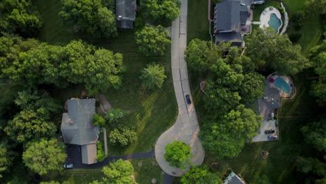 A-car-drives-down-the-street-in-a-nice-neighborhood-and-pulls-into-a-driveway-as-the-aerial-camera-spins-in-a-360