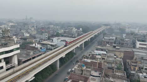 Vista-Aérea-Del-Tren-De-Metro-De-La-Línea-Naranja-Cerca-De-McLeod-Road-En-Lahore-En-Una-Vía-Elevada-Con-Contaminación-Del-Aire-Brumoso-En-El-Fondo