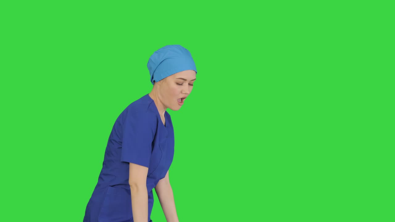 una mujer médica sonriente en uniforme azul bailando y aplaudiendo en una pantalla verde, clave de croma