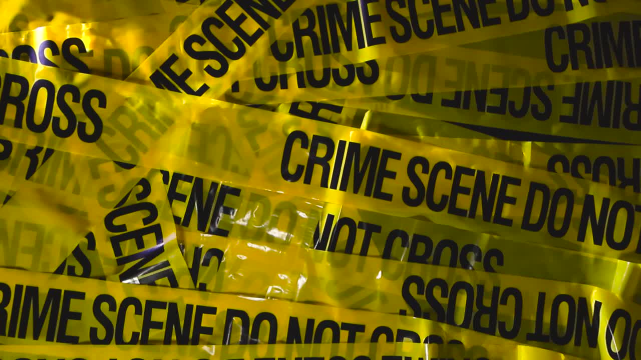 Studio close up of layered yellow forensic barrier tape as the camera lifts upward, revealing bold warning text, strong shadows, and vibrant color under directional lighting