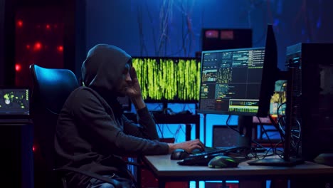 male software developer in a hood sitting at the computer in the office at night and programming some project website