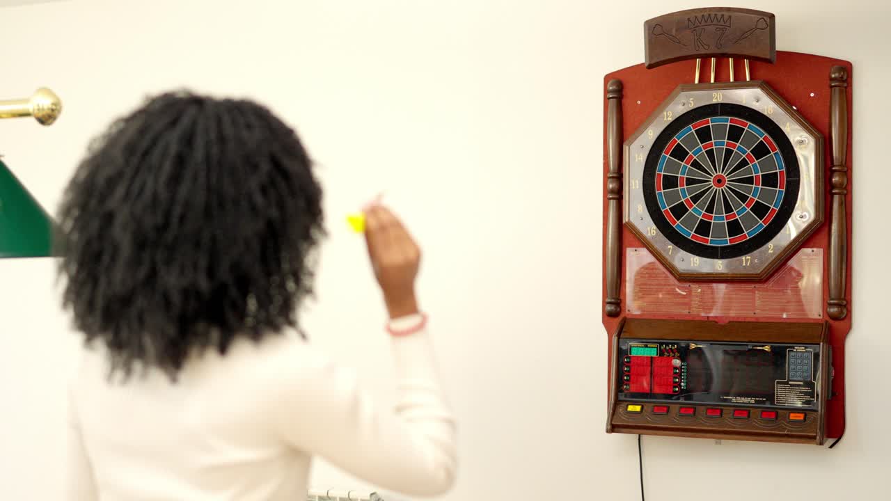 Rear view of an african woman playing darts at home