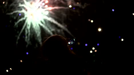la niña toma fotos de fuegos artificiales en un teléfono móvil. silueta en el fondo del cielo iluminado por luces