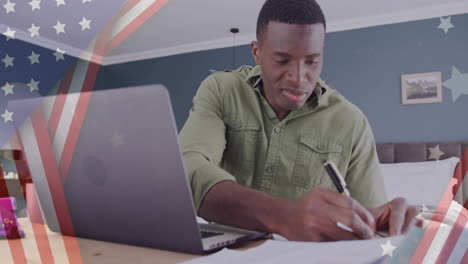 animation of flag of usa over happy african american businessman using laptop