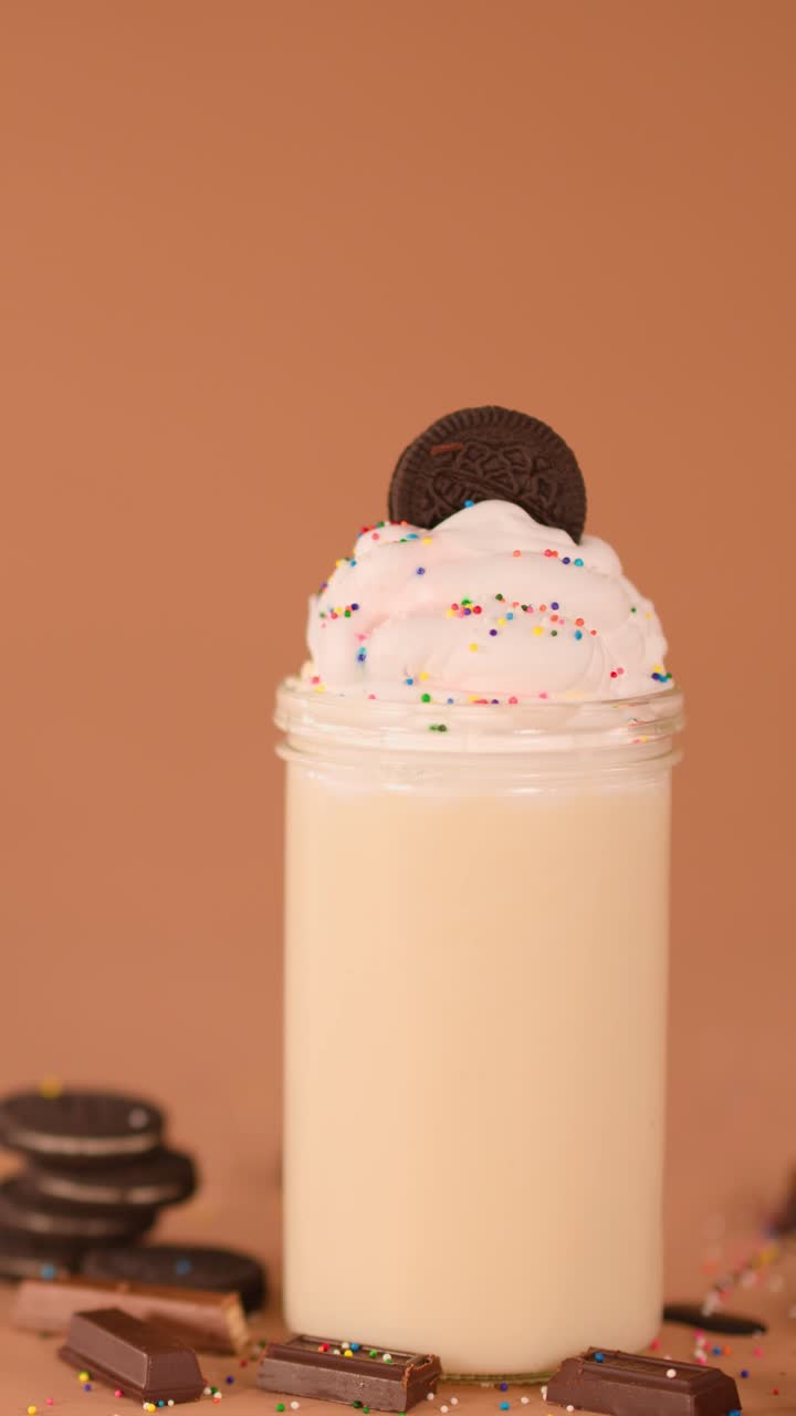 Primo piano di un milkshake guarnito con un biscotto e una cannuccia a righe su uno sfondo caldo, movimento minimo della telecamera