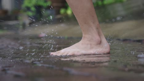 low angle of female bare feet jumping and playing on water puddle on the raining day, pouring rain on the street side walking path way, fun time splashing water, jumping goofy around, care free vibe