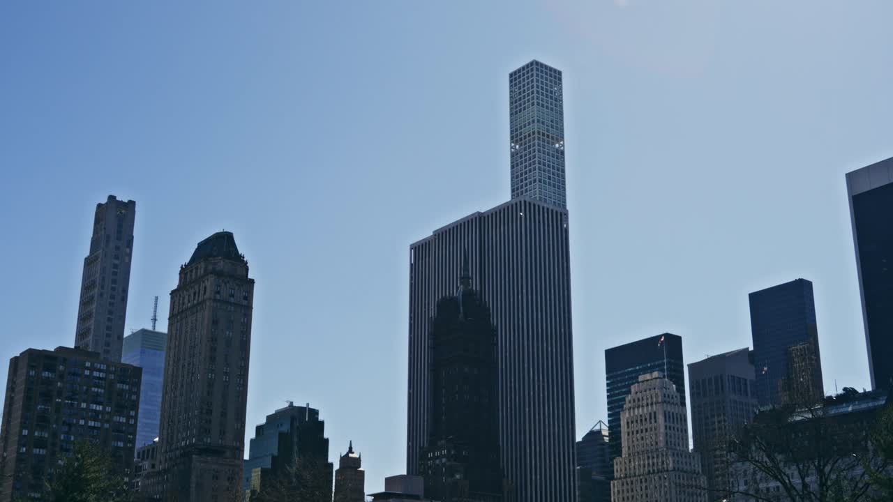 The Manhattan skyline rises under a clear blue sky, featuring the iconic 432 Park Avenue tower among historic and modern skyscrapers