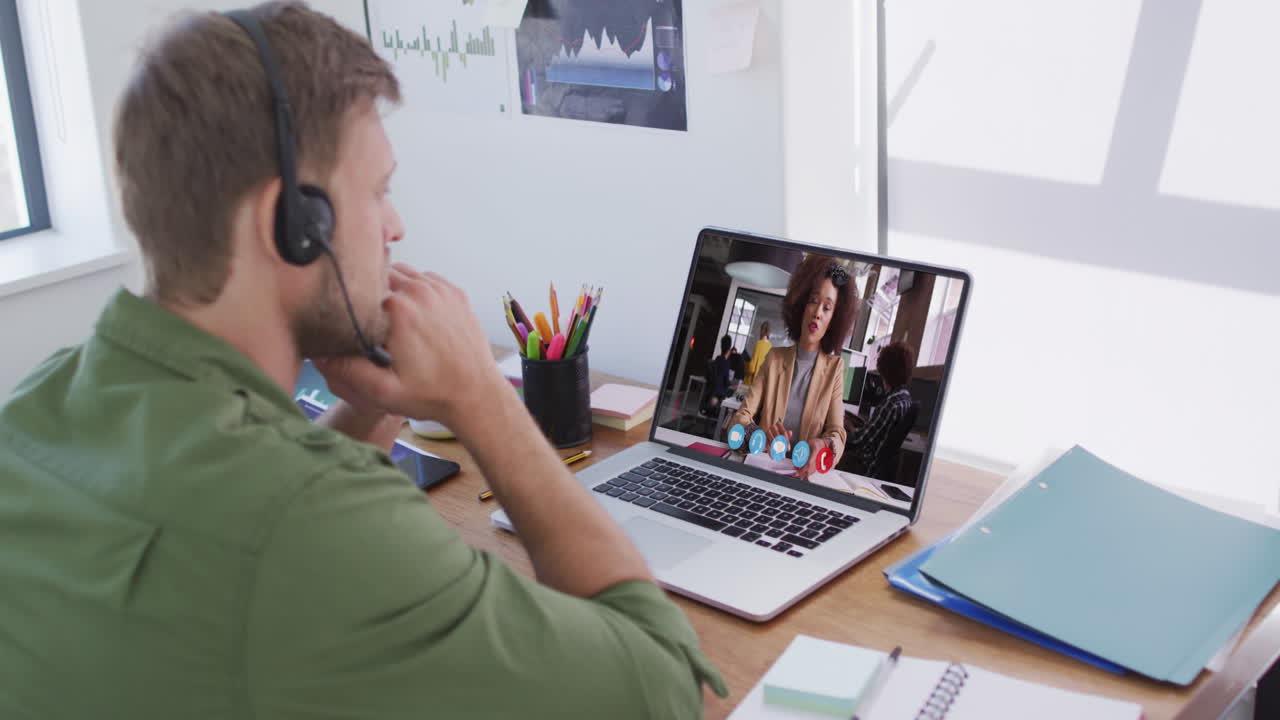 En kaukasisk mand med telefonheadset holder et videomøde med en kvindelig kollega på sin bærbare computer på kontoret.