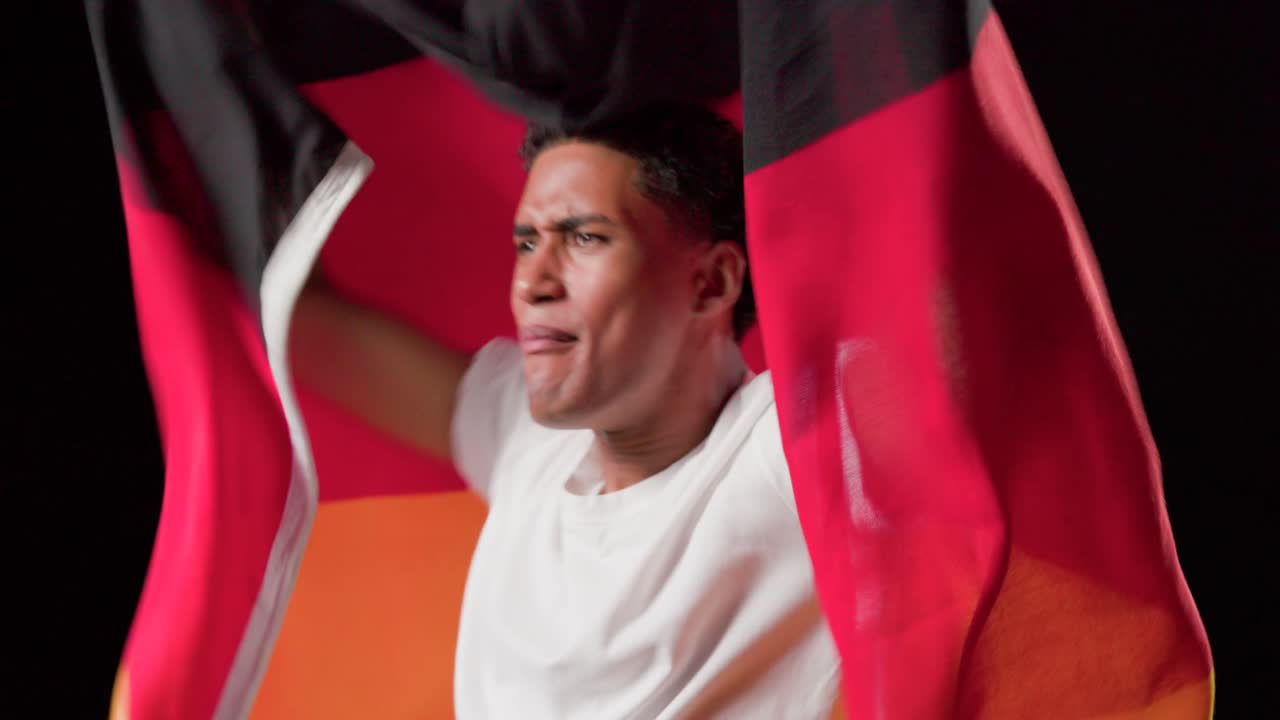 Uomo afroamericano che entra in uno studio buio, mentre drappeggia, srotola, solleva, sventola e raduna con una bandiera tricolore.