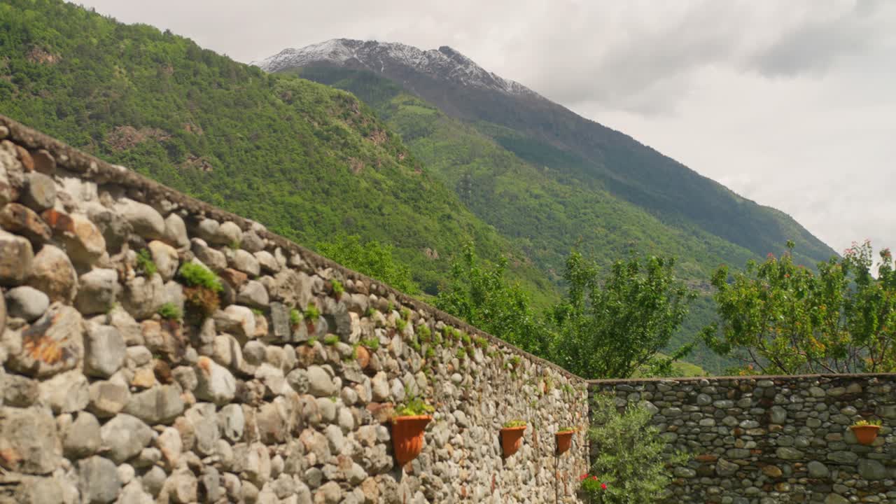 Maestosa cima montuosa innevata che domina pendii verdi e muri in pietra di una tenuta vinicola locale.